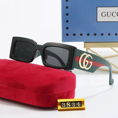 Black square sunglasses with gold hinges lying on a red velvet tray next to a pale blue presentation box