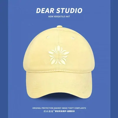 A pale yellow cap with a white embroidered flower at the front, photographed against a printed blue card