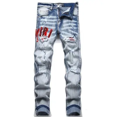 Light-wash jeans laid flat with distressing at the knee and red embroidery running down the thigh