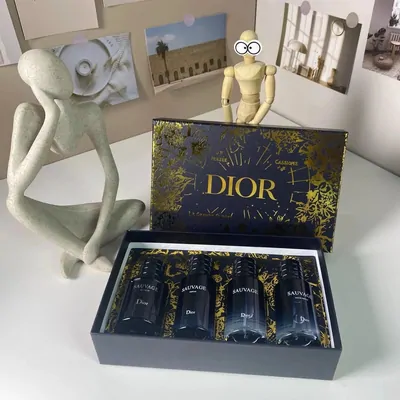 A navy and gold gift box holding four miniature fragrance bottles, with two small ornaments standing beside it